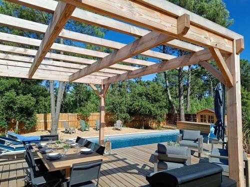 une pergola en bois avec une table et des chaises à côté d'une piscine dans l'établissement MAISON 4 CHAMBRES PISCINE CHENAL DES DUNES, à Saint-Jean-de-Monts