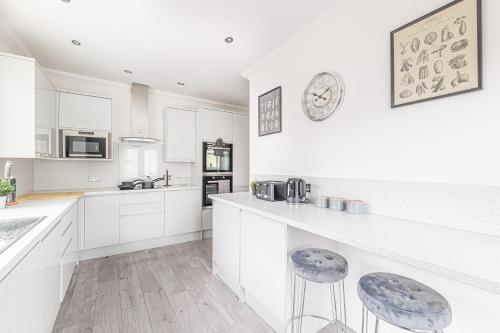 a white kitchen with white cabinets and stools at Luxury 4 Bedroom Apartment Southsea - Free Parking in Portsmouth
