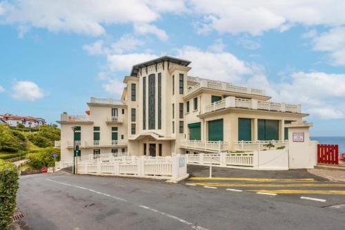 un grand bâtiment avec une clôture blanche devant une rue dans l'établissement Guethary sur la plage, à Guéthary
