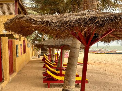 a group of chairs and a straw umbrella on a beach at Maison Couleur Passion in Nianing