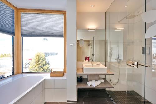 a bathroom with a tub and a sink and a window at Genuss- & Aktivhotel Sonnenburg in Riezlern