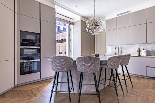 une cuisine avec des armoires blanches et une table avec des tabourets dans l'établissement Appartement Avenue Montaigne - Paris Champs Elysées, à Paris