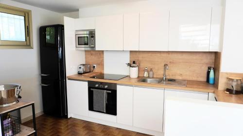 a kitchen with white cabinets and a black refrigerator at Villa avec Rooftop, Jacuzzi & vue mer by Palmazur in Mandelieu-la-Napoule