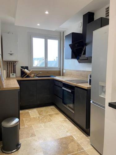 - une cuisine avec des armoires noires et un réfrigérateur dans l'établissement Appartement cosy - Le Verdun, à Caen