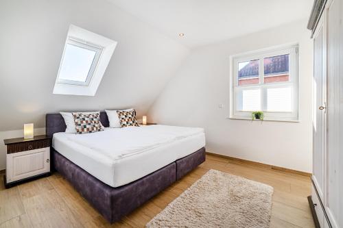 a white bedroom with a bed and two windows at Mühlenblick 04 in Greetsiel
