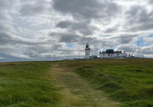 a dirt road leading to a light house with a lighthouse at Loop Head Lighthouse Attendant's Cottage in Kilbaha