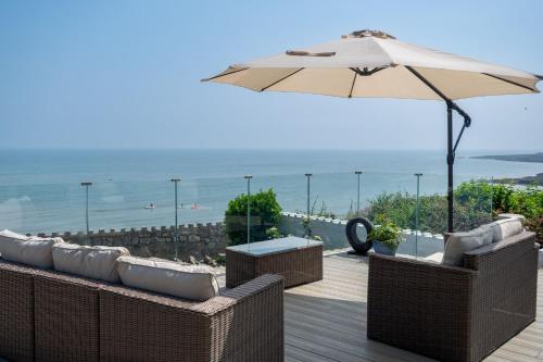 a patio with chairs and an umbrella and the ocean at Sea Spray in Moelfre