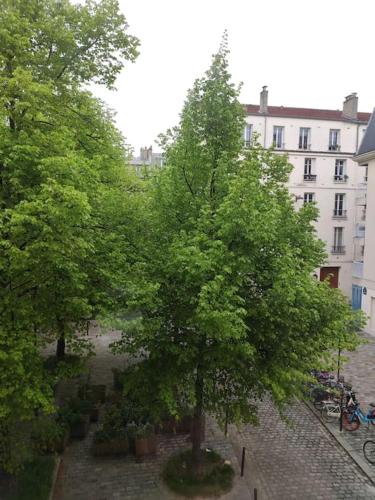 un arbre dans une cour devant un bâtiment dans l'établissement Bel Appartement avec vue square - Paris Nation - 3 Voyageurs, à Paris
