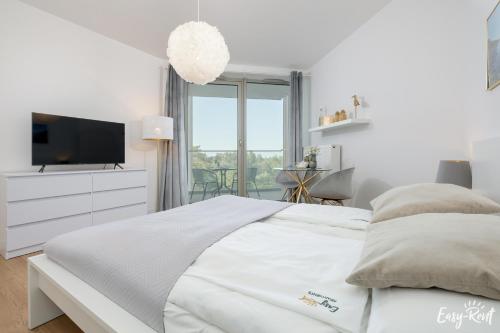 a white bedroom with a bed and a tv at Apartamenty Pinea z widokiem na morze Easy - Rent Apartments in Pobierowo