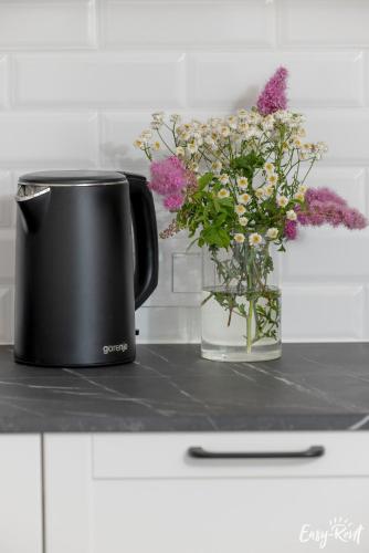 a black coffee mug and a vase of flowers on a counter at Apartamenty Pinea z widokiem na morze Easy - Rent Apartments in Pobierowo