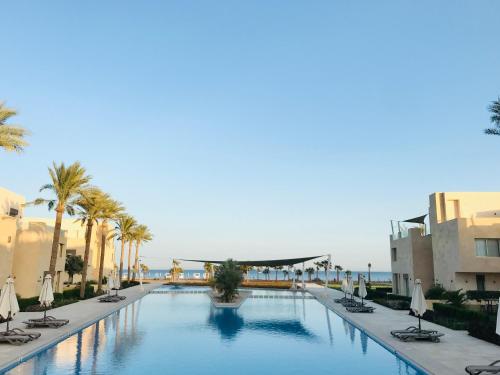 a large swimming pool with chairs and palm trees at Mangroovy - Elgouna Authentic Designer shared home 2 BDR each with private bathroom for Kitesurfers with Pool View & Beach Access in Hurghada