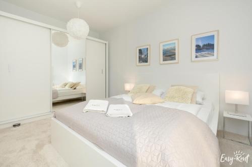 a white bedroom with a large white bed and a mirror at Apartamenty Pinea z widokiem na morze Easy - Rent Apartments in Pobierowo