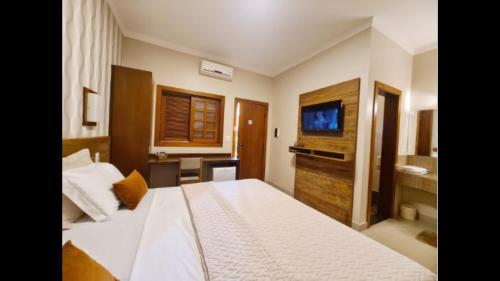 a bedroom with a white bed and a television at Hotel Pousada Santa Rita in Ribeirão Preto