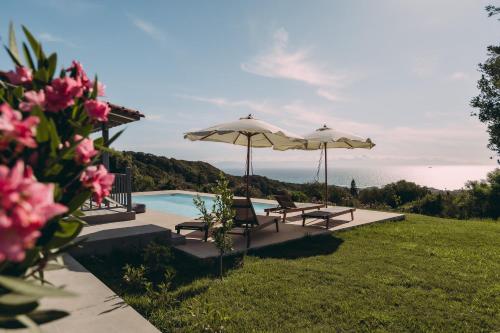 a pool with two umbrellas and chairs next to the water at Villa Filokalia With Exceptional View - Happy Rentals in Kastro Kyllini