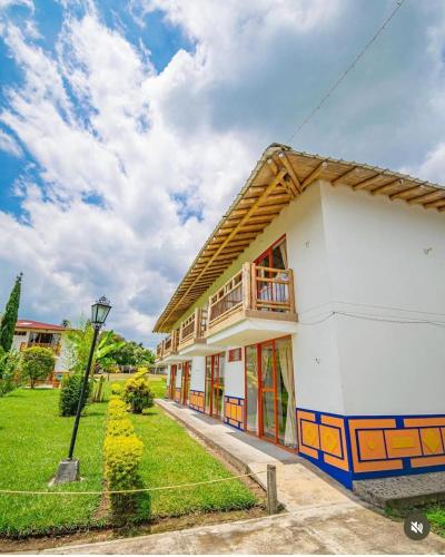 a white building with a balcony and a green yard at Hotel Campestre La Aldea Cabaña Pijao in Montenegro