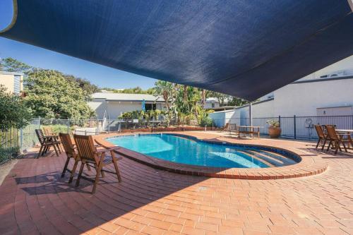 a swimming pool with chairs and a blue umbrella at Banksia Retreat, A couple's sanctuary on Aldinga Beach in Aldinga Beach