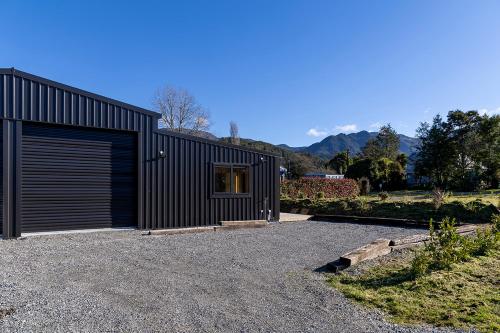 a black house with a garage on a gravel driveway at Blackball Connection in Blackball