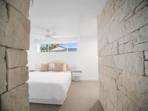 a bedroom with a white bed and a stone wall at Luxury Home in the Vale in Berkeley Vale
