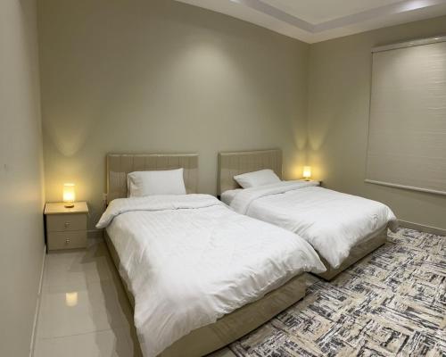 two beds in a bedroom with white sheets and lamps at شقة فاخرة قرب الحرم النبوي in Al Madinah