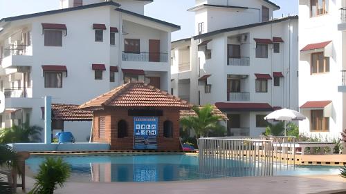 a small building next to a swimming pool in front of buildings at Ronne's Little Baga service apartments in Goa