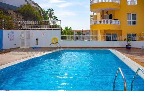 a swimming pool in front of a house with a yellow building at Seaside Escape 2bed By Dream Homes Tenerife in Puerto de Santiago