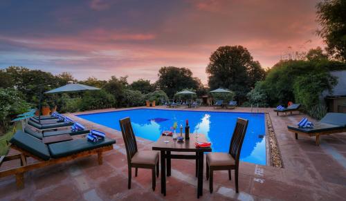 un patio con tavolo e sedie accanto alla piscina di The Pugmark, A Wildlife Resort a Sawai Madhopur