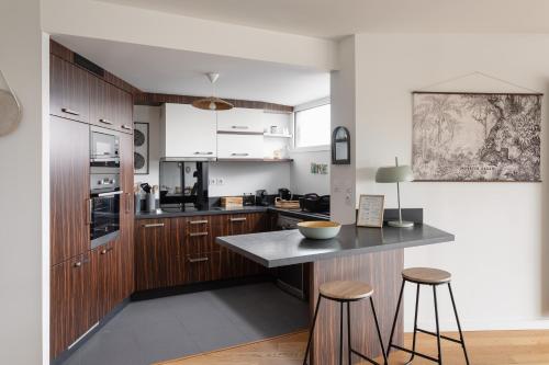 une cuisine avec des armoires en bois et un comptoir avec des tabourets dans l'établissement Namasté - Bel appt pour 5 avec terrasse parking, à Rennes