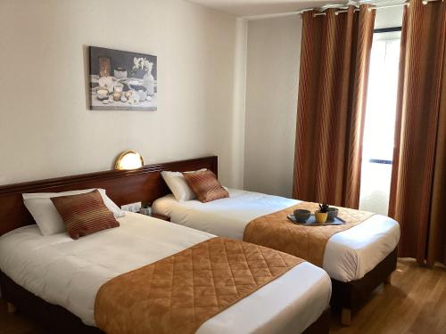 a hotel room with two beds and a window at Hôtel Angelic in Lourdes