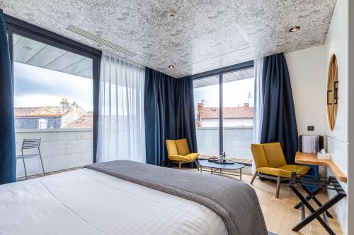 a bedroom with a bed and chairs and windows at Hotel Le Saint Gelais in Angoulême