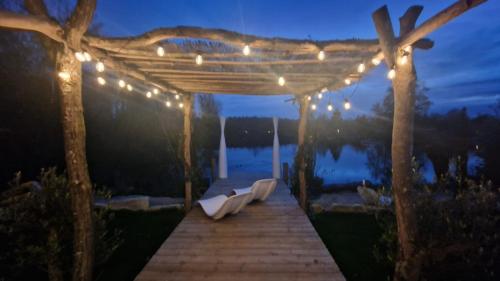 a wooden boardwalk with a pergola with lights at KÄBANE 54, Lodge avec spa au bord de l'eau in Prouilly