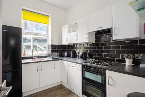 a kitchen with white cabinets and a black tile wall at Strawberry One - 3 en-suite bedrooms, Private Parking - Harrogate Holiday Apartments in Harrogate
