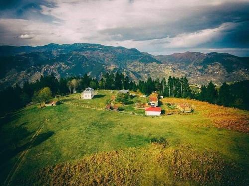 a green field with a house on a hill with mountains at Yavuzyılmaz Tesisleri in Macka