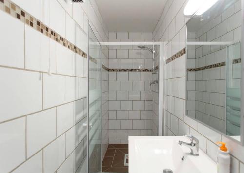 La salle de bains est pourvue de carrelage blanc, d'un lavabo et d'une douche. dans l'établissement A 5' de la plage, à Cannes
