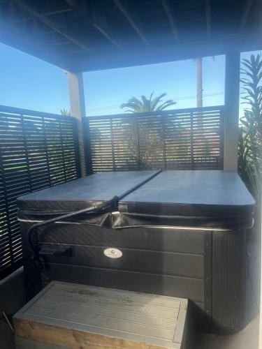 a balcony with a bed and a window with palm trees at Beach house with a pool in Waihi Beach