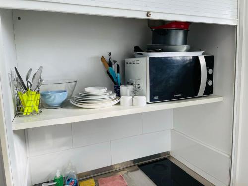un four micro-ondes sur une étagère avec des assiettes et des ustensiles dans l'établissement S6 Bel Appartement 10min centre paris stade de France, à Saint-Denis