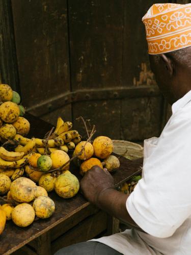 a man sitting in front of a table filled with fruit at Melia Zanzibar in Kiwengwa
