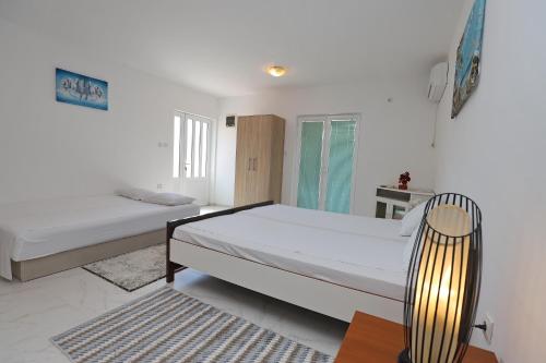 a white bedroom with two beds and a chair at Apartmani Amra in Ivanovići