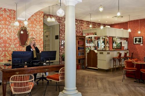 a woman talking on a phone at a table in a room at Hotel Le Grimaldi by Happyculture in Nice