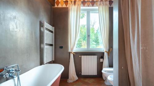 a bathroom with a tub and a toilet and a window at CASCINA MOGLIA 8&1, Emma Villas in Carpeneto