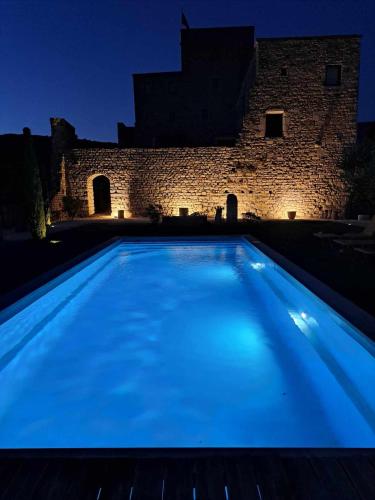 - une piscine bleue en face d'un bâtiment la nuit dans l'établissement Chateau de Sainte Jalle, à Sainte-Jalle