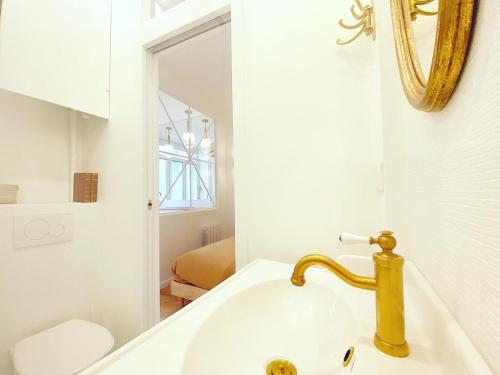 La salle de bains est pourvue d'un lavabo avec un robinet en or et un miroir. dans l'établissement Magnifique appartement a Paris - FLAT-GUEST, à Paris