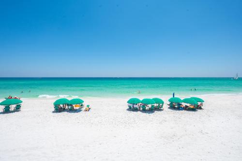 a group of people sitting under green umbrellas on a beach at The Surf Shack in Destin
