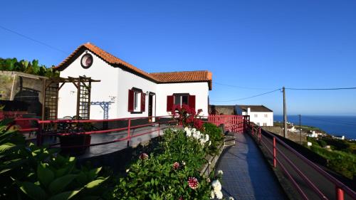 a small white house with red doors and flowers at Quinta dos Cinco Sentidos in Feteira Grande