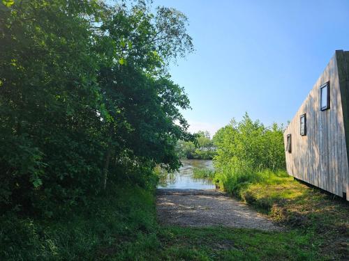 a dirt road next to a river with a building at Tiny House De Klyster in Westergeest