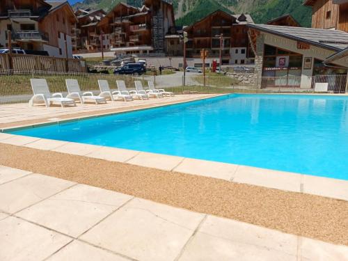 une piscine bleue avec des chaises longues et un bâtiment dans l'établissement Les Mélèzes d'Or - Proche des pistes de ski, aux Orres