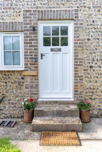 a white door on a brick building with two potted plants at Redshank Cottage in West Dean
