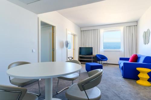 a living room with a white table and blue chairs at Golden Tulip Marseille Euromed in Marseille