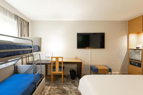a hotel room with a bed and a desk with a television at Novotel Macon Nord - Porte de Bourgogne in Mâcon