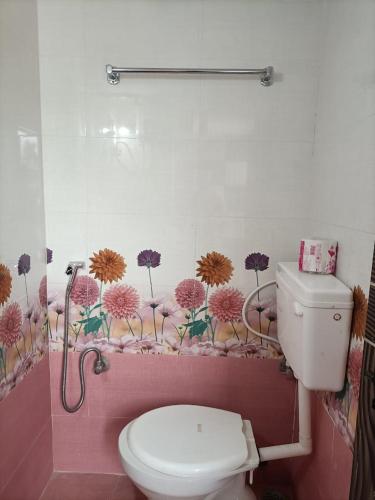 a bathroom with a toilet and flowers on the wall at VIDYA Homestay in Hampi