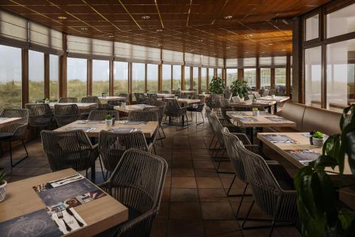 a restaurant with tables and chairs and windows at WestCord Strandhotel Seeduyn in Oost-Vlieland